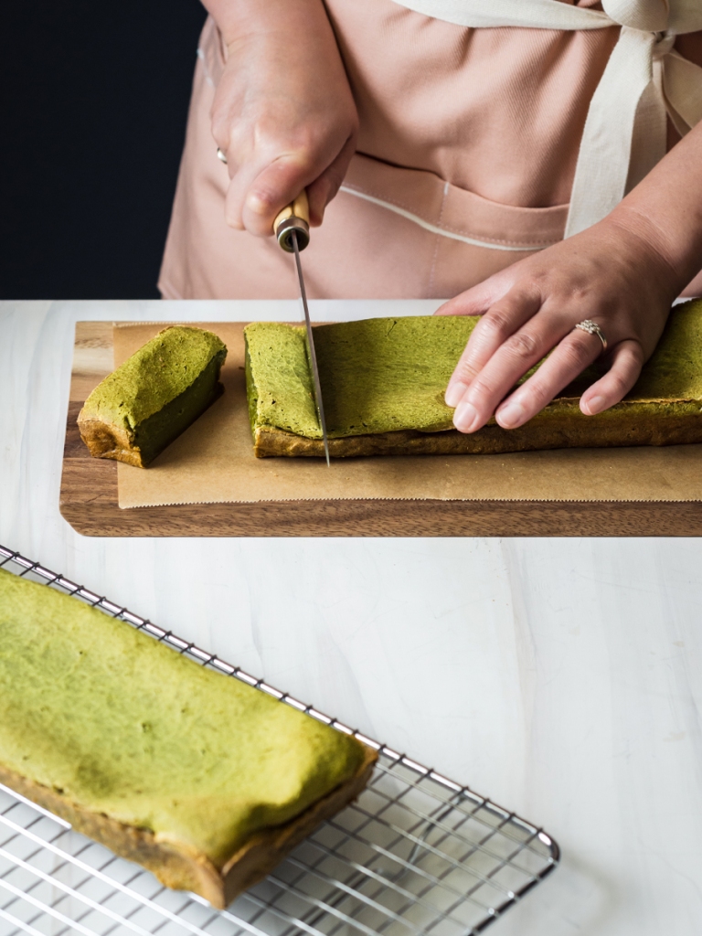 hands holding a knife to cut baked matcha mochi cake loaf into stripes first