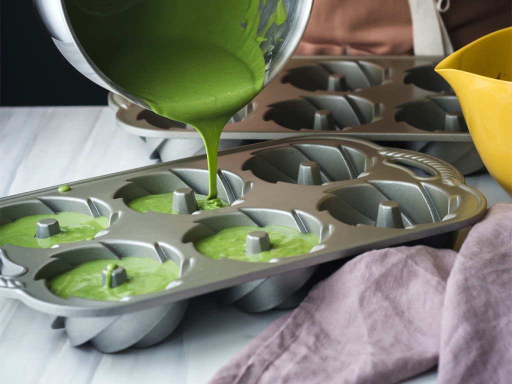 pouring matcha mochi cake batter into two mini bundt pans on a marble-patterned background 